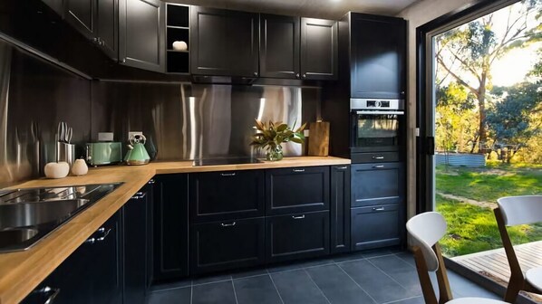 Una cocina moderna con armarios oscuros, electrodomésticos de acero inoxidable y encimera de madera.