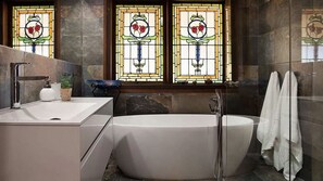 A modern bathroom with a freestanding bathtub, a vanity with a sink, and a window with stained glass featuring roses.