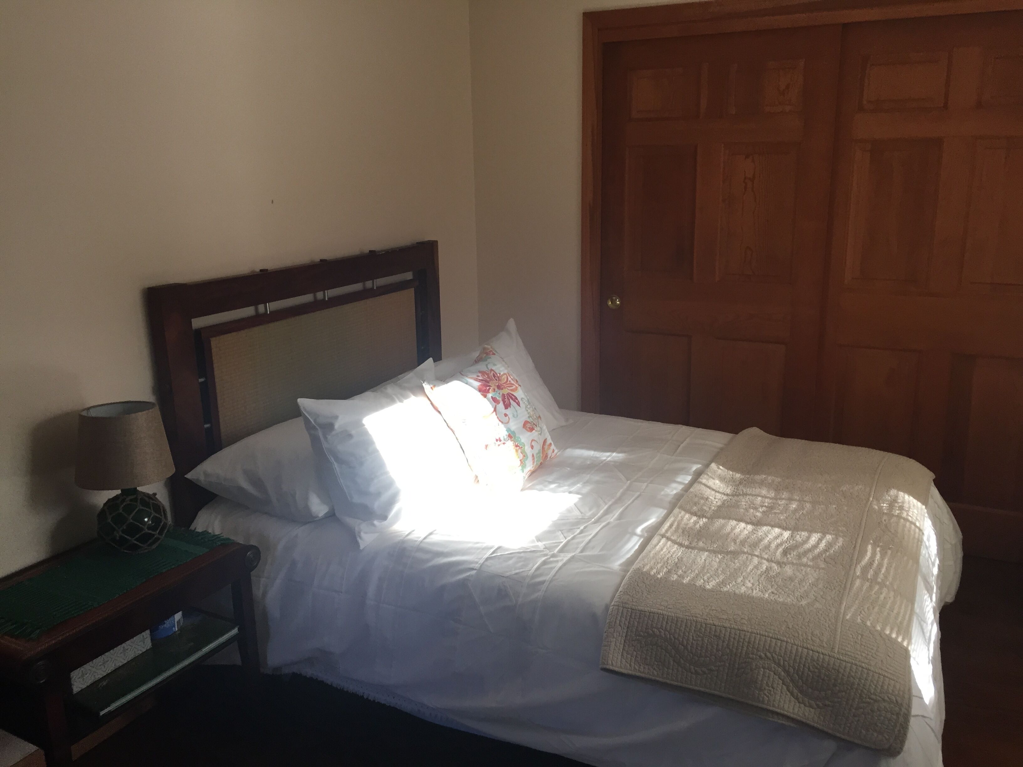 A neatly made bed with white linens and a decorative pillow, a bedside lamp, and a wooden nightstand with a decorative item.