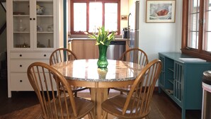 A dining area with a round table, four wooden chairs, a green vase with flowers, a cabinet with glass doors, and a kitchen in the background. - Secluded Chatham Cape Cod House Stage Harbor Area (Chatham)