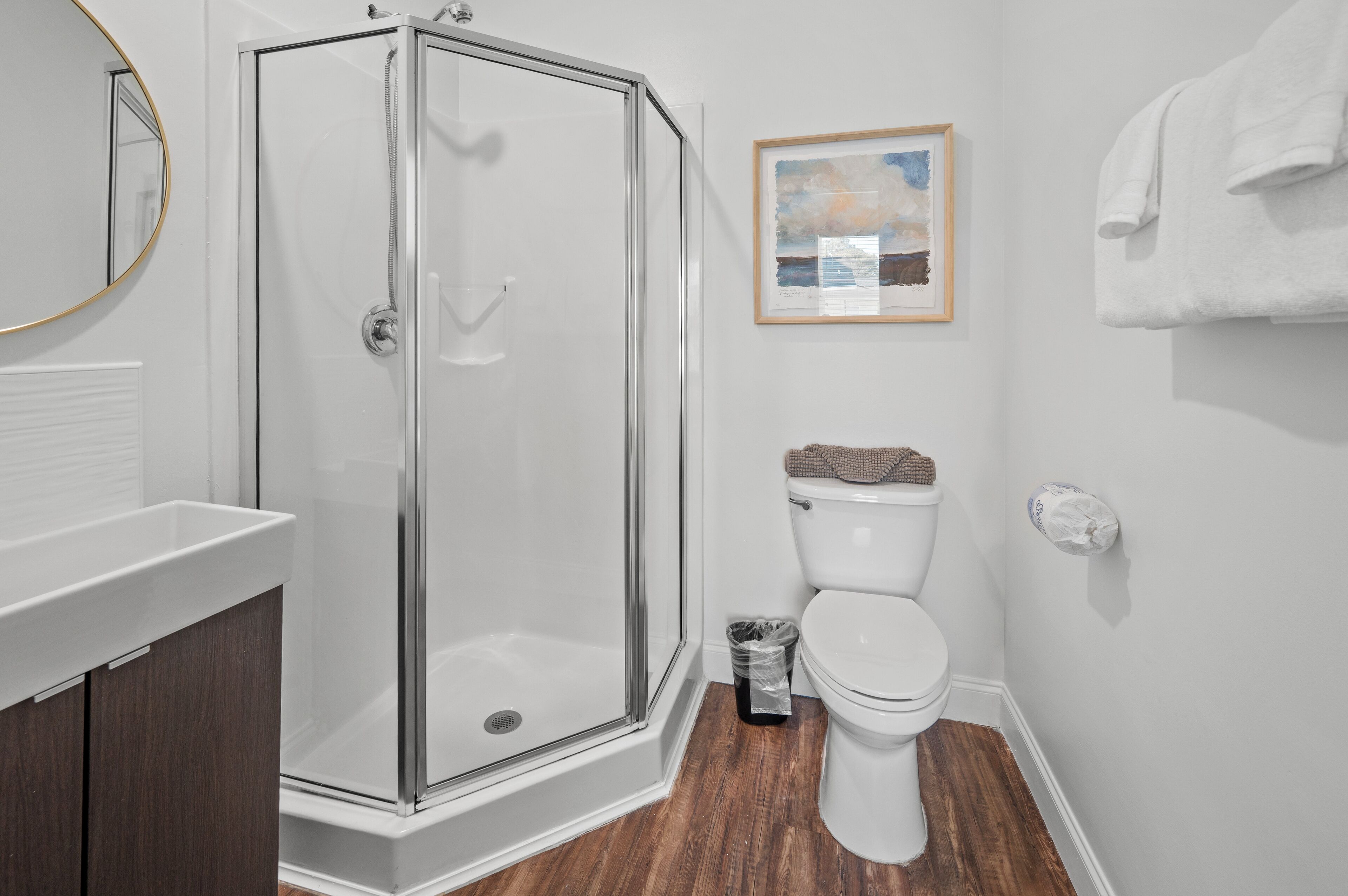 Un baño con cabina de ducha de vidrio, un inodoro blanco, una obra de arte enmarcada en la pared y un perchero para toallas.