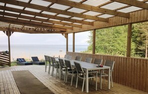 Un espacio de comedor al aire libre techado con vistas al mar, muelle de madera y estructura de pérgola.