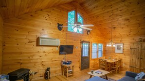 Un intérieur de chalet chaleureux avec des murs en bois, un ventilateur de plafond, un téléviseur, un coin repas et un canapé.