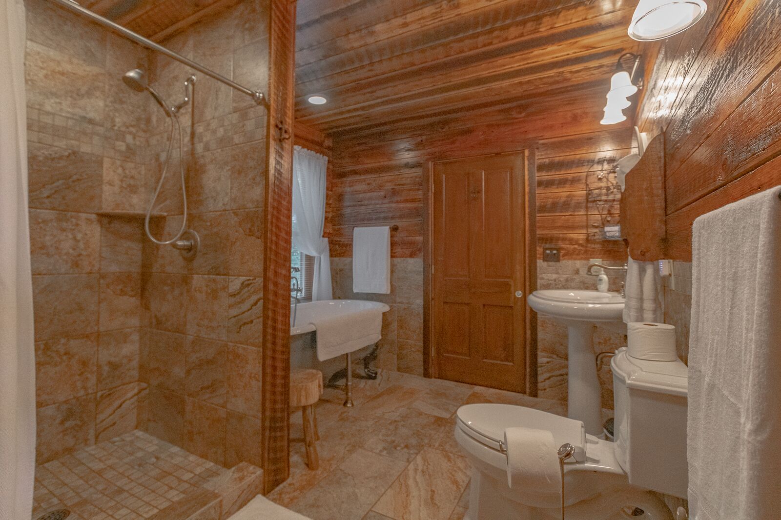 A bathroom with a shower, sink, toilet, and wooden walls.