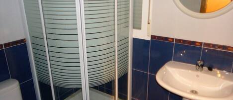 A bathroom with a glass shower enclosure, a sink, and blue-tiled walls.