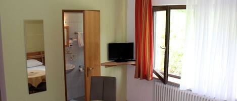 Une chambre d’hôtel avec un lit, une petite table, une télévision, une salle de bain et une fenêtre avec des rideaux.