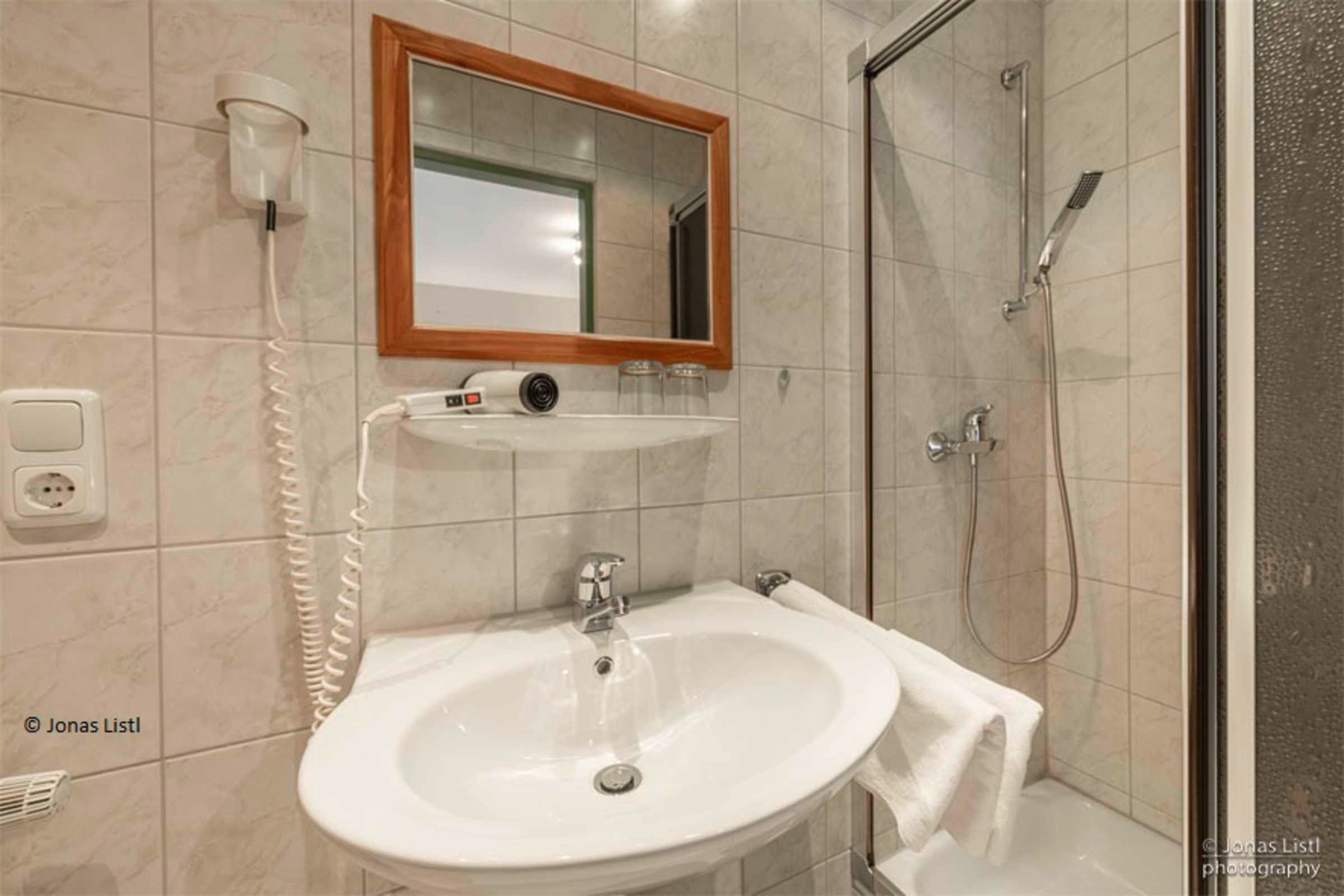 Ein Badezimmer mit Waschbecken, Spiegel, Föhn und Dusche.