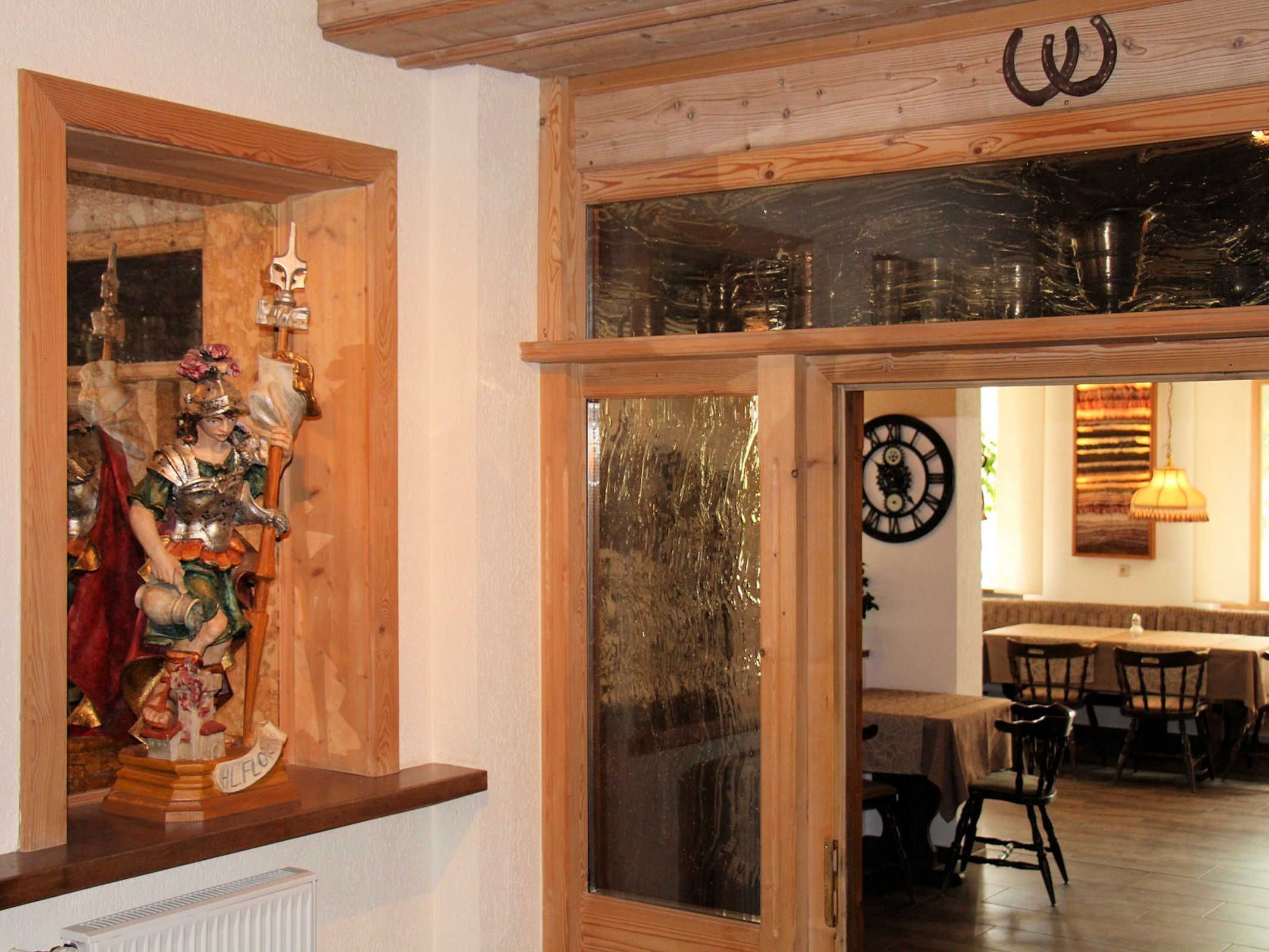 A room with a wooden-framed window, a clock on the wall, and a dining area with chairs and a table.