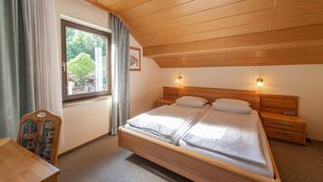 A bedroom with a wooden bed, two bedside tables, a nightstand, a chair, and a window with curtains.