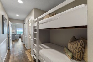 Una cama litera con cabecera identificada con el nombre "BUNKY" y una pequeña zona de estar con una silla y una mesa.