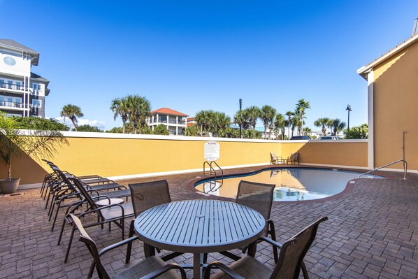 A poolside area with a round table and chairs, a swimming pool, and a building with balconies in the background.