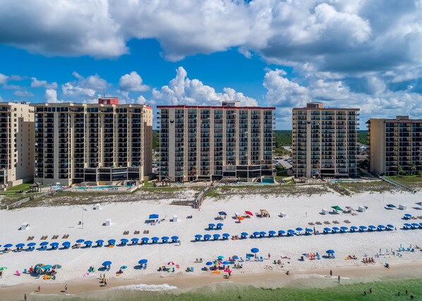Un hôtel situé en bord de mer, composé de plusieurs immeubles de grande hauteur, doté d’une plage de sable et de nombreux parasols.