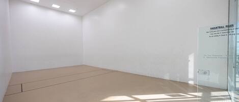 Amplia habitación bien iluminada con un muro de vidrio que muestra las reglas del raquetball.
