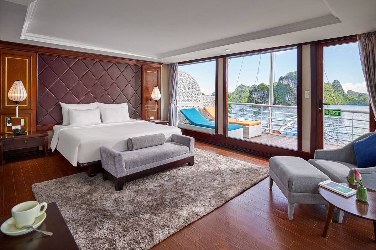Une chambre d’hôtel moderne dotée d’un grand lit, d’un coin salon avec vue sur l’eau et d’un balcon avec une balustrade.