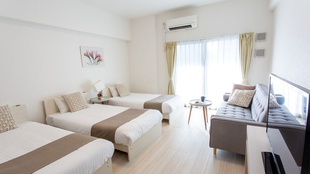 A hotel room with two beds, a sofa, a TV, and a window with curtains.