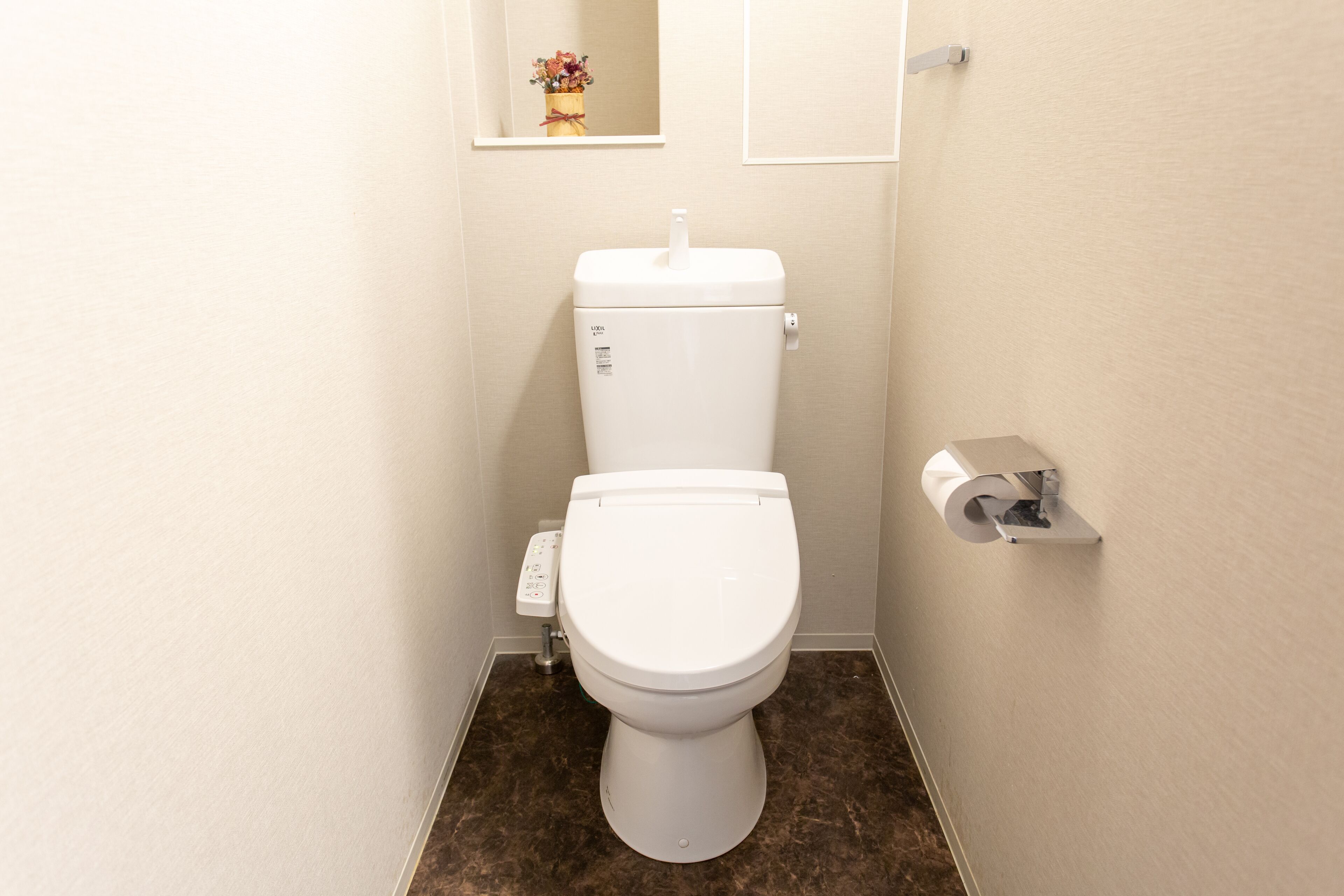 A small, clean bathroom with a toilet, a toilet paper holder, and a wall-mounted shelf with a small decorative item.