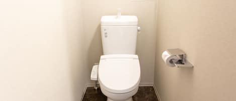 A small, clean bathroom with a toilet, a toilet paper holder, and a wall-mounted shelf with a small decorative item.