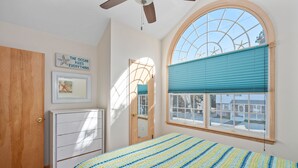 A bedroom with a bed, a dresser, a ceiling fan, a window with blinds, and a wall with a starfish decoration.