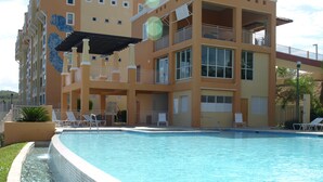 A swimming pool with a tiled edge, surrounded by a building with balconies and a covered area. - PENTHOUSE CONDO | BEAUTIFUL | 3 BEDS | 3 BATHS | 2 LEVELS | MAGNIFICENT VIEWS (Fajardo)