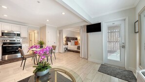 A modern apartment with a kitchen, dining area, and living room. It includes a flat-screen TV mounted on the wall, a dining table with chairs, and a bed with a headboard. - 🌷Steps to Siesta Beach, Chic Studio, Pool & Patio (Siesta Key)