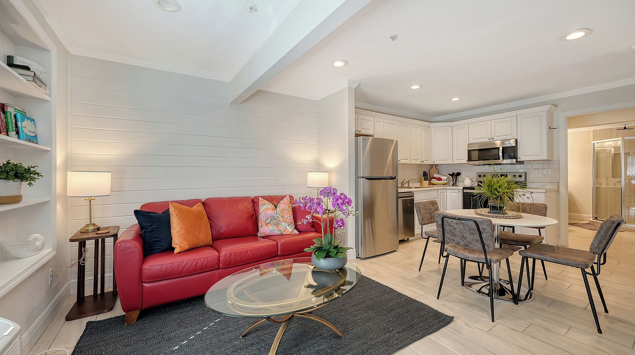 A modern living room with a red sofa, a glass coffee table, and a dining area with a white table and chairs.