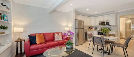 A modern living room with a red sofa, a glass coffee table, and a dining area with a white table and chairs.
