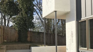 Una casa moderna con fachada de ladrillo blanco, un porche cubierto y una valla de madera al fondo.