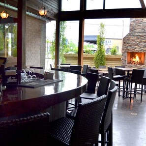 Un área de bar al aire libre con chimenea de piedra, sillas de mimbre y vista a un edificio de fondo.