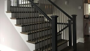 Una escalera con barandillas negras y peldaños de madera, que conduce a una plataforma con interruptor de luz y toma de corriente.