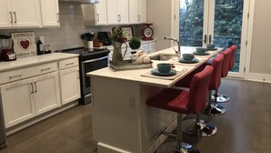 Una cocina moderna con muebles blancos, una isla central con taburetes y vistas al exterior a través de una puerta de cristal.