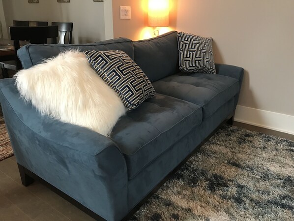 Un sofá azul oscuro con almohadones estampados y una manta blanca y mullida.