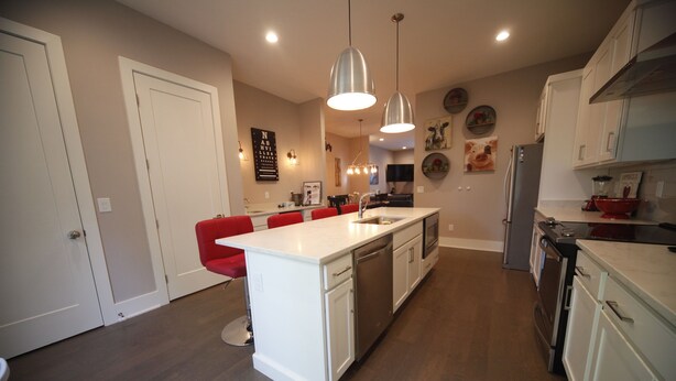 Una cocina moderna con armarios blancos, una isla central, taburetes de bar rojos, electrodomésticos de acero inoxidable e iluminación colgante.