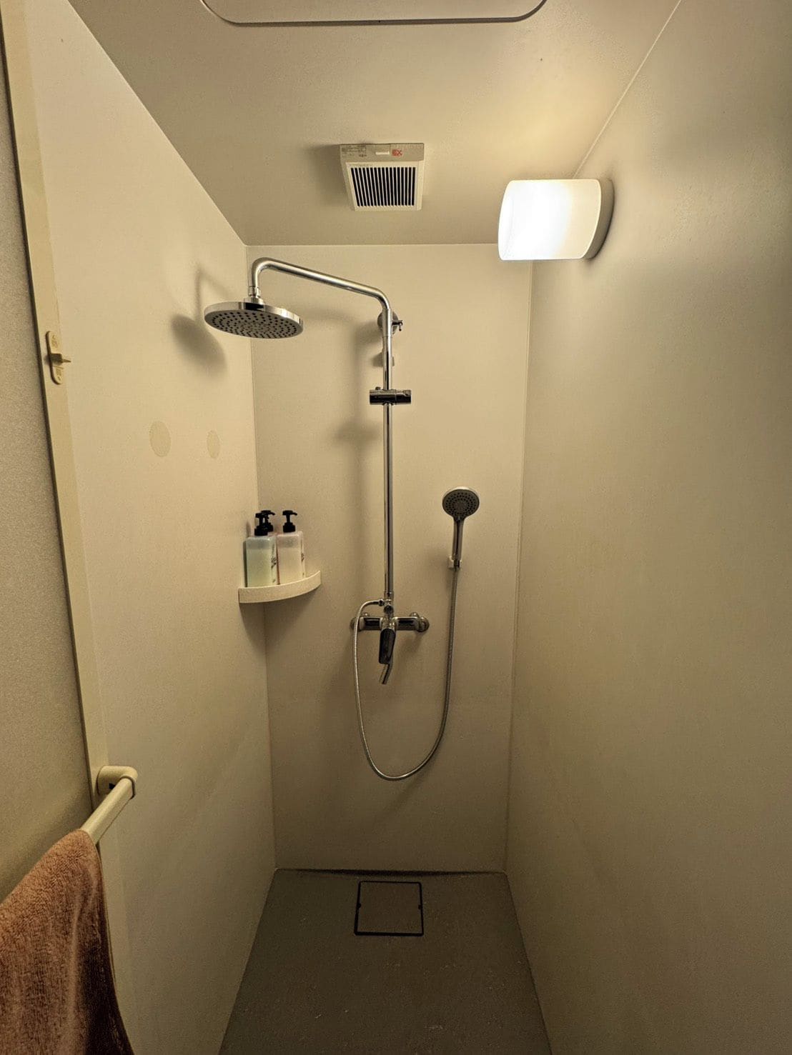 Un petit espace de douche fermé, équipé d’un pommeau de douche à main, d’un robinet mural et d’un système de ventilation.
