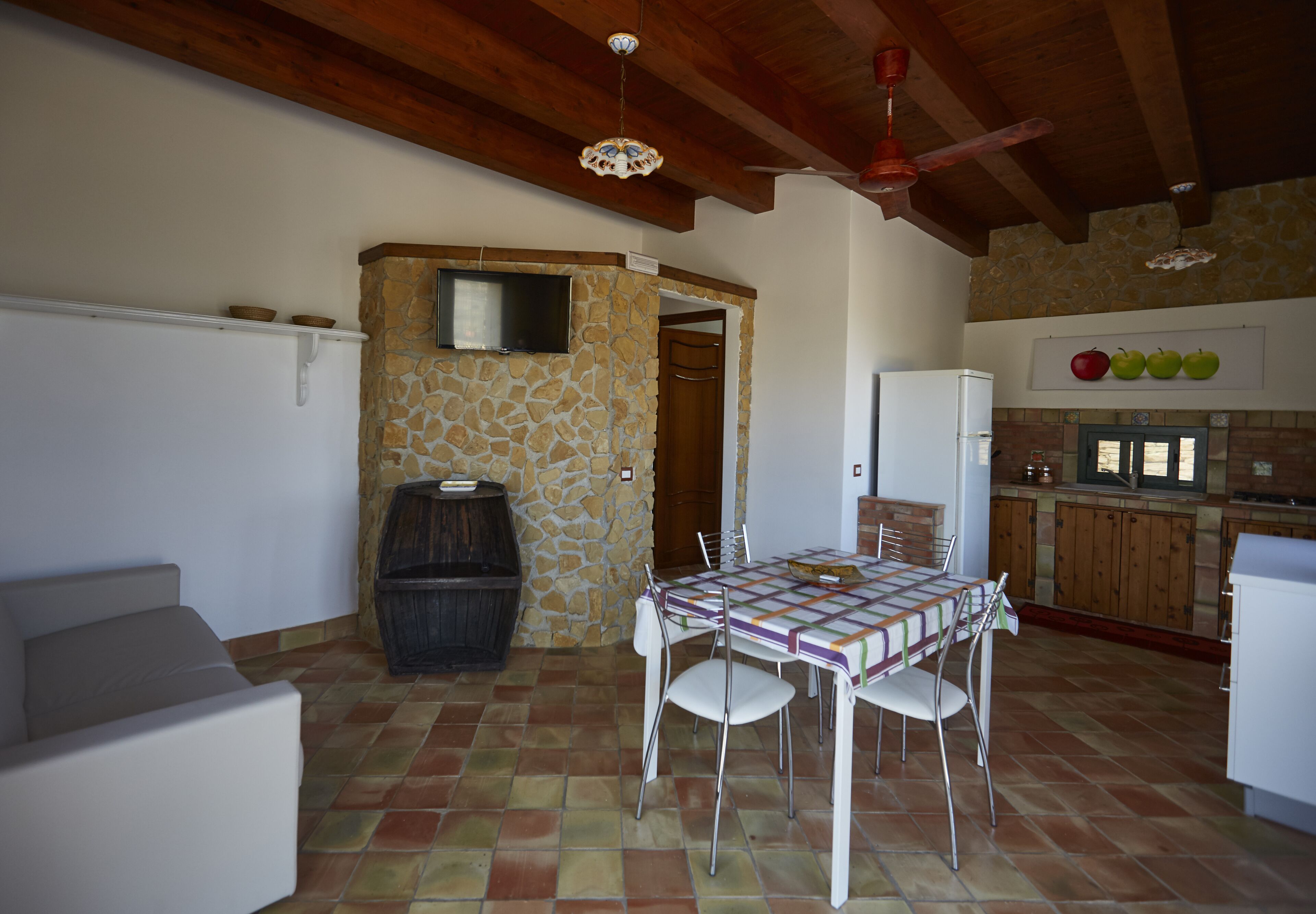 Un espace repas comprenant une table et des chaises, un mur en pierre, un téléviseur et un coin cuisine avec des placards et un réfrigérateur.