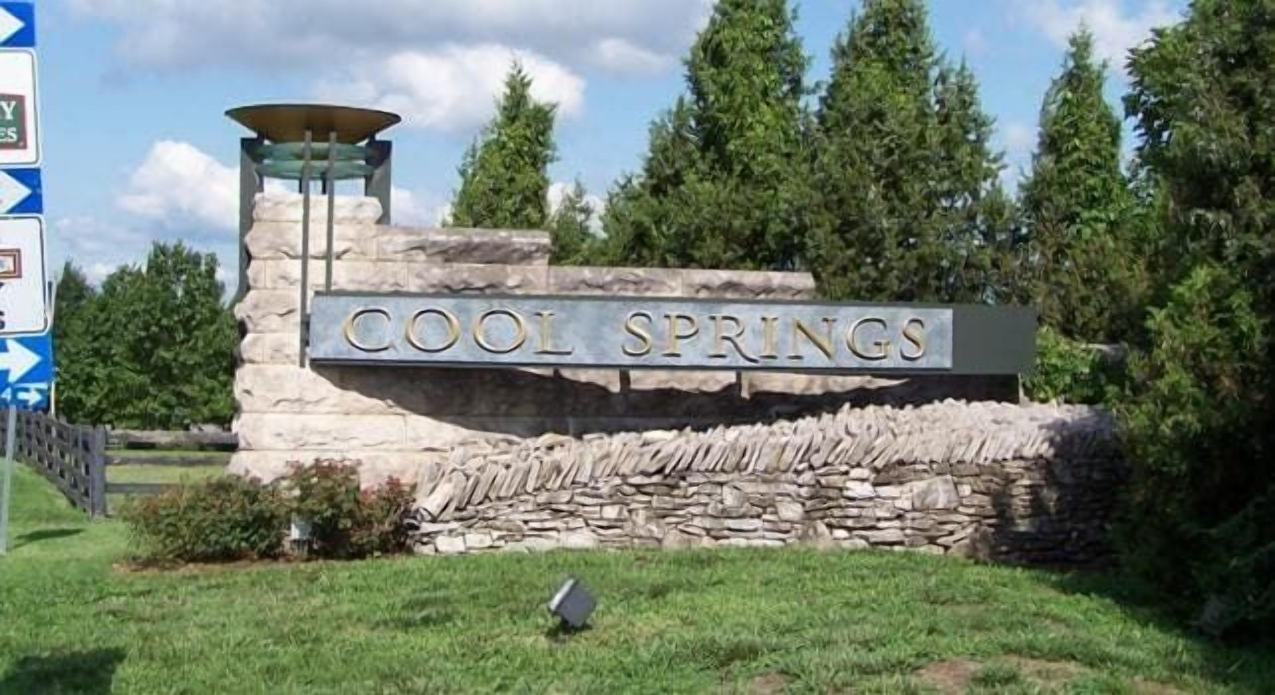 Un cartello in pietra con la scritta "COOL SPRINGS" davanti a un muro di pietra e una struttura metallica.