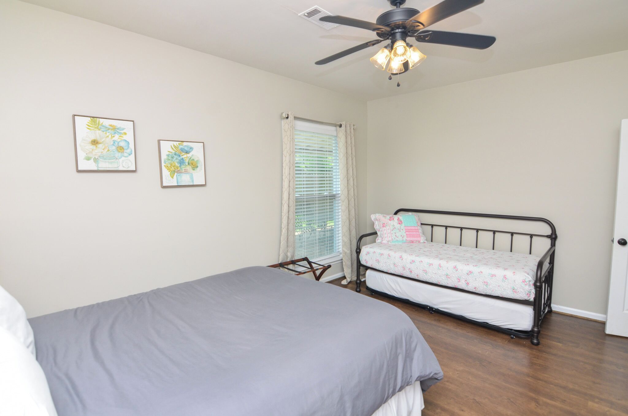 A bedroom with a bed, a ceiling fan, and two framed floral artworks on the wall.