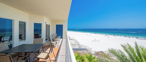 Un balcon avec une table et des chaises, donnant sur une plage de sable blanc et une eau d’un bleu cristallin.