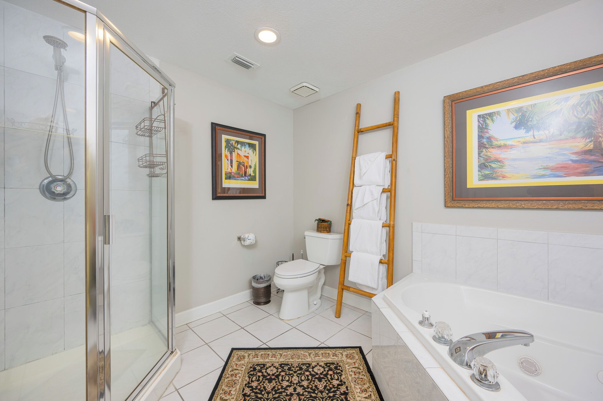 A bathroom with a glass shower enclosure, a toilet, a bathtub, and a framed painting on the wall.