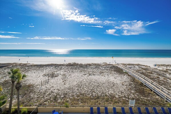 A beach with a wooden boardwalk, palm trees, and a clear blue sky.