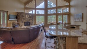 A spacious living area with a stone fireplace, a large windowed wall, a leather sofa, and a kitchen island. - Luxury Cabin - views, location, perfect for families, 4 miles from Breckenridge (Blue River)