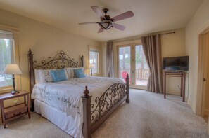 A bedroom with a bed, a ceiling fan, a TV on a stand, and a window with curtains.