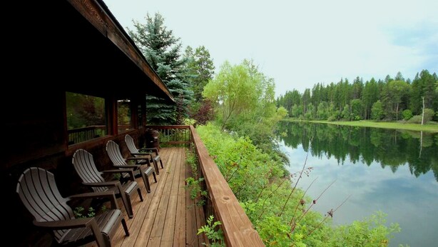 Eine Holzterrasse mit Adirondack-Stühlen, mit Blick auf einen stillen See, umgeben von Bäumen.