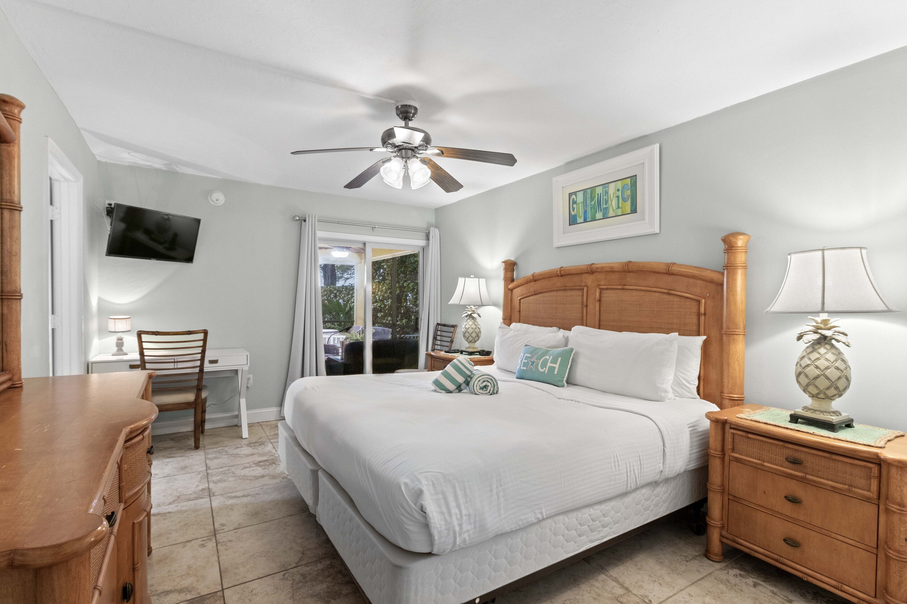 A bedroom with a bed, wooden nightstand, desk, chair, and a ceiling fan.