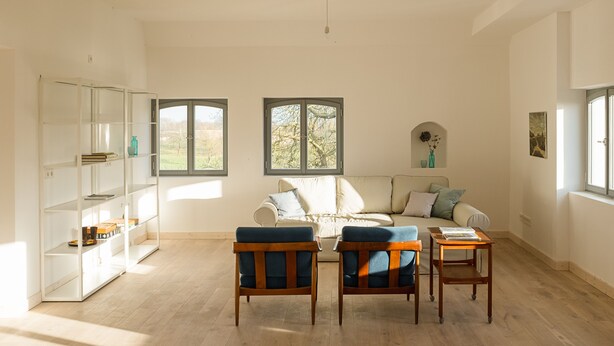 Un salón amplio con un sofá blanco, dos sillas de madera, una mesita de madera y un estante blanco.