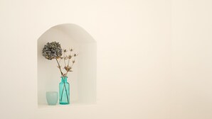 Un salón minimalista con un hueco arqueado blanco que contiene un jarrón con flores secas y un pequeño cuenco.