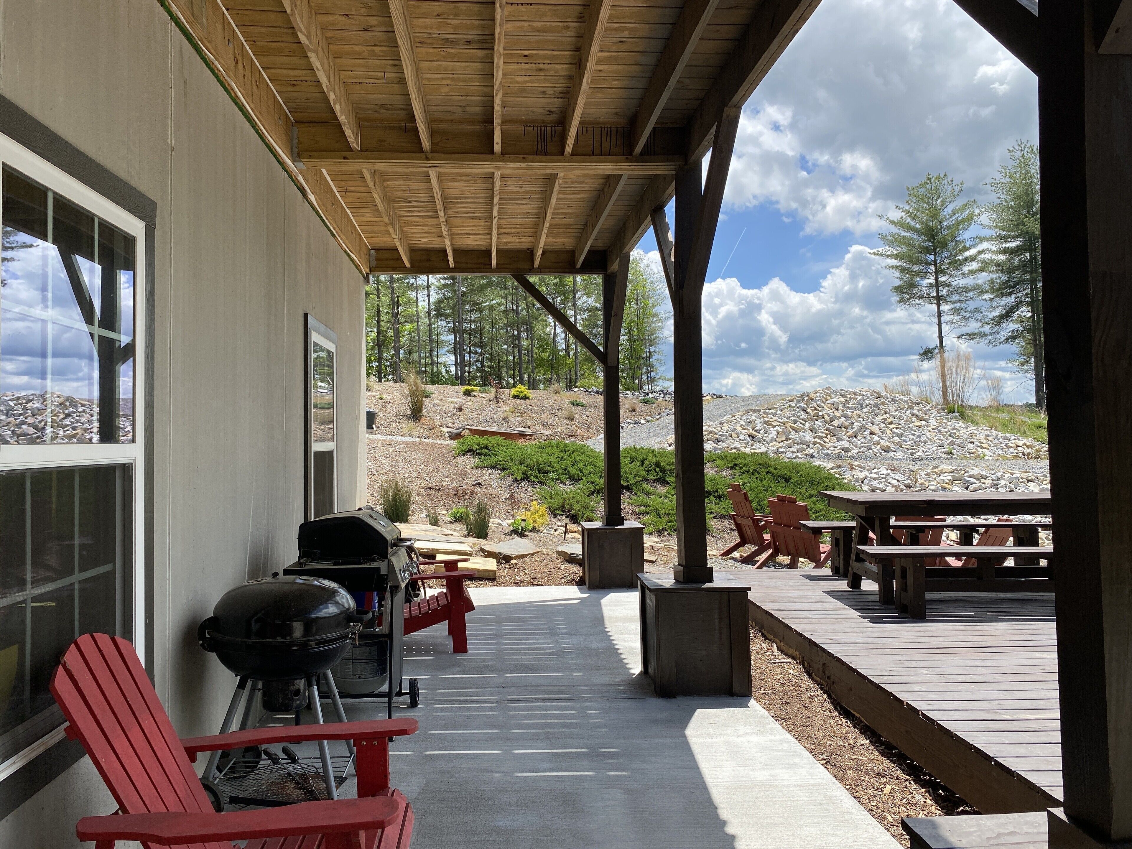 A covered patio with a barbecue grill, red Adirondack chairs, and a picnic table.