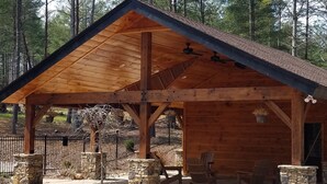 Ein hölzerner Pavillon mit steinernen Säulen, Sitzgelegenheiten im Freien und einem umzäunten Bereich.