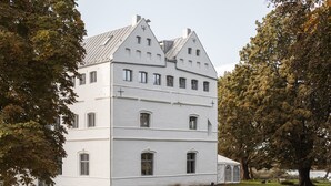 A large, white, multi-story building with a symmetrical facade, several windows, and a prominent cross on the roof. - Apartment Gut Üselitz on Rügen - 2. Upper floor right 1 (Poseritz)