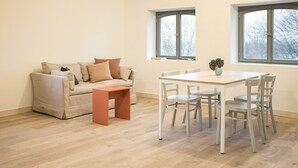 A living room with a beige sofa, a wooden coffee table, and a dining table with four chairs. There are two windows providing natural light. - Apartment Gut Üselitz on Rügen - 2. Upper floor right 1 (Poseritz)