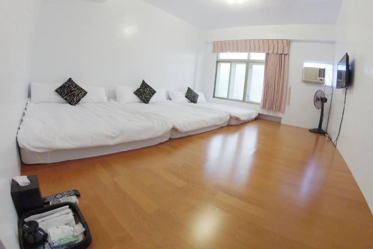 A room with a large bed, a flat-screen TV, and a window with curtains.